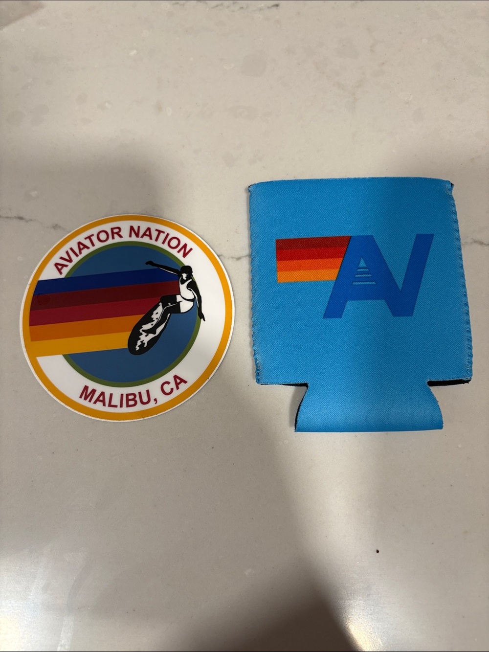 Aviator Nation blue can koozie and rainbow surfer sticker
